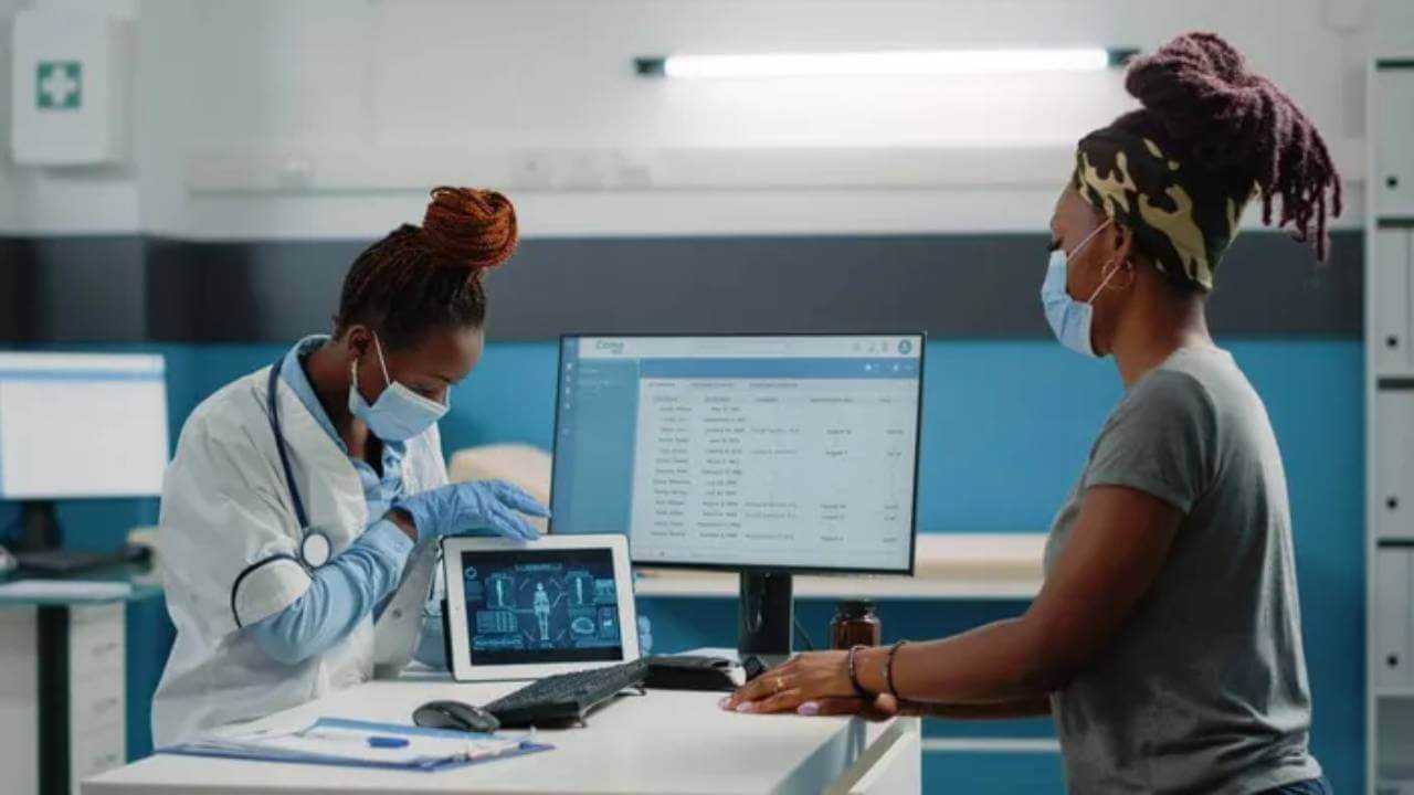 Healthtech professional with a patient looking at a computer screen and tablet.