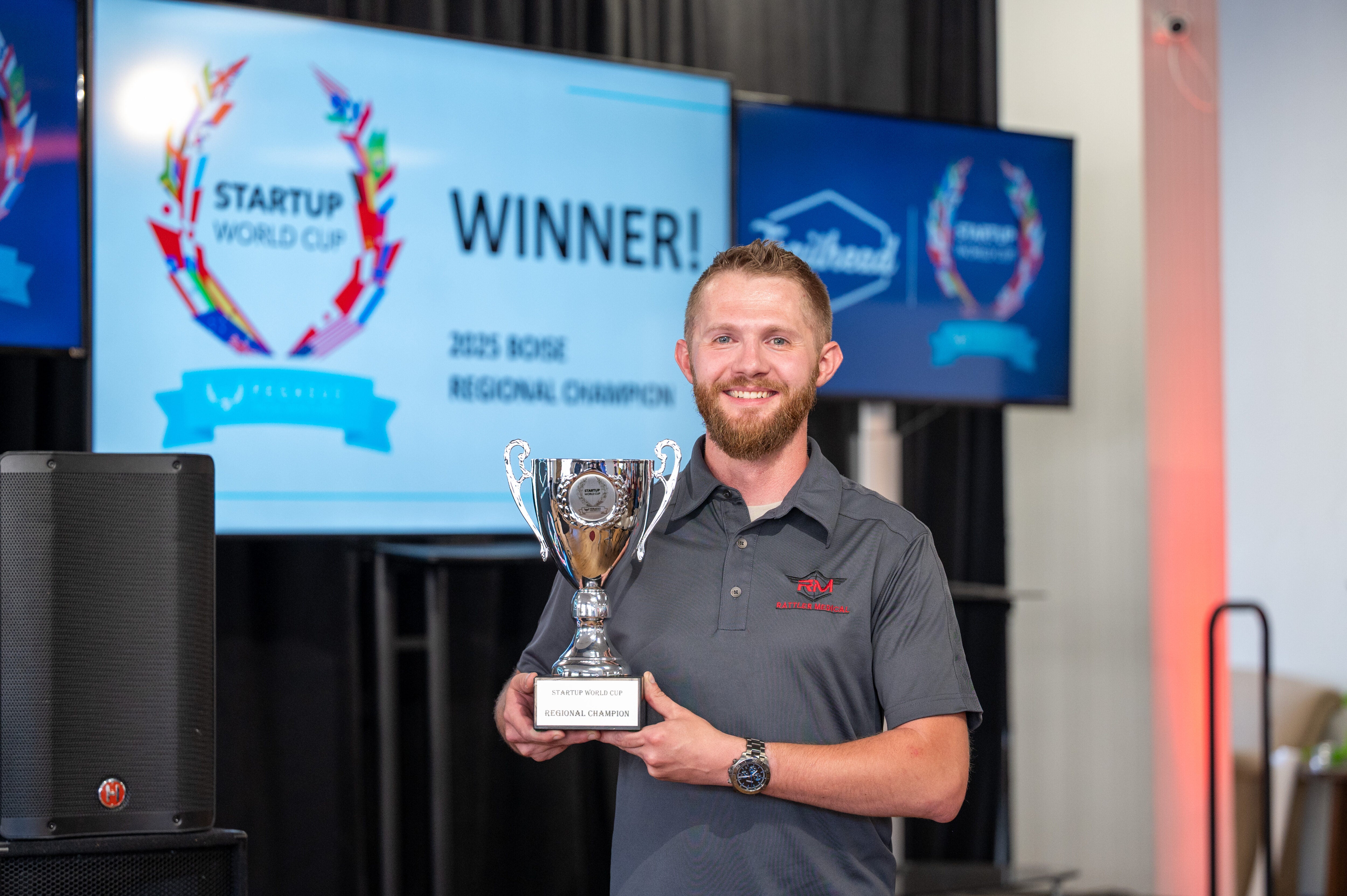 Donald Young smiles for the camera, wearing a grey Rattler Medical polo and holding a silver trophy