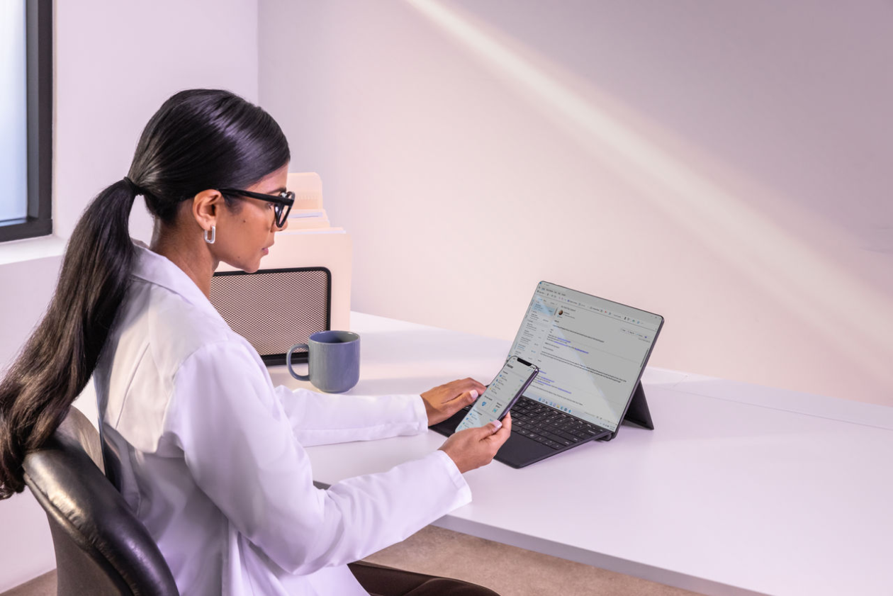 Woman sitting at desk with laptop open and cell phone in hand.