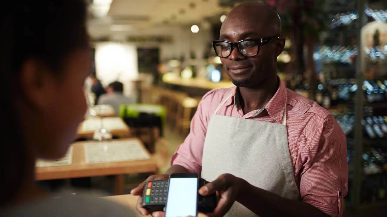 Restaurant worker takes digital smartphone payment on POS machine. 