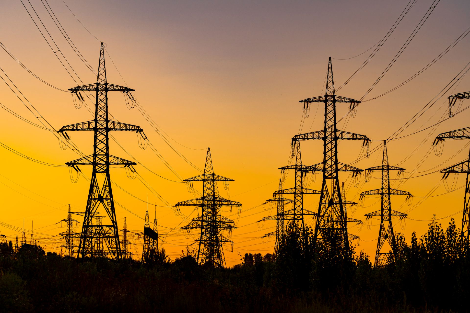 Silhouettes of power lines and towers against a vibrant orange and purple sunset sky.
