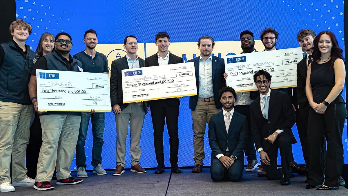 Thirteen students stand on a stage holding three checks.