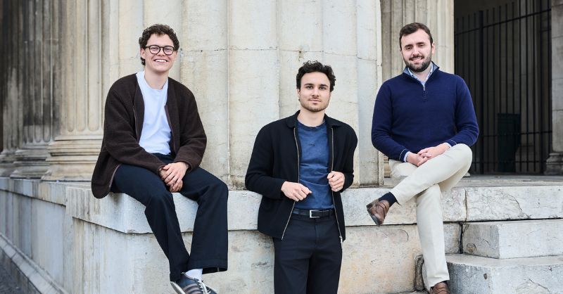 Three men stand outside looking at the camera