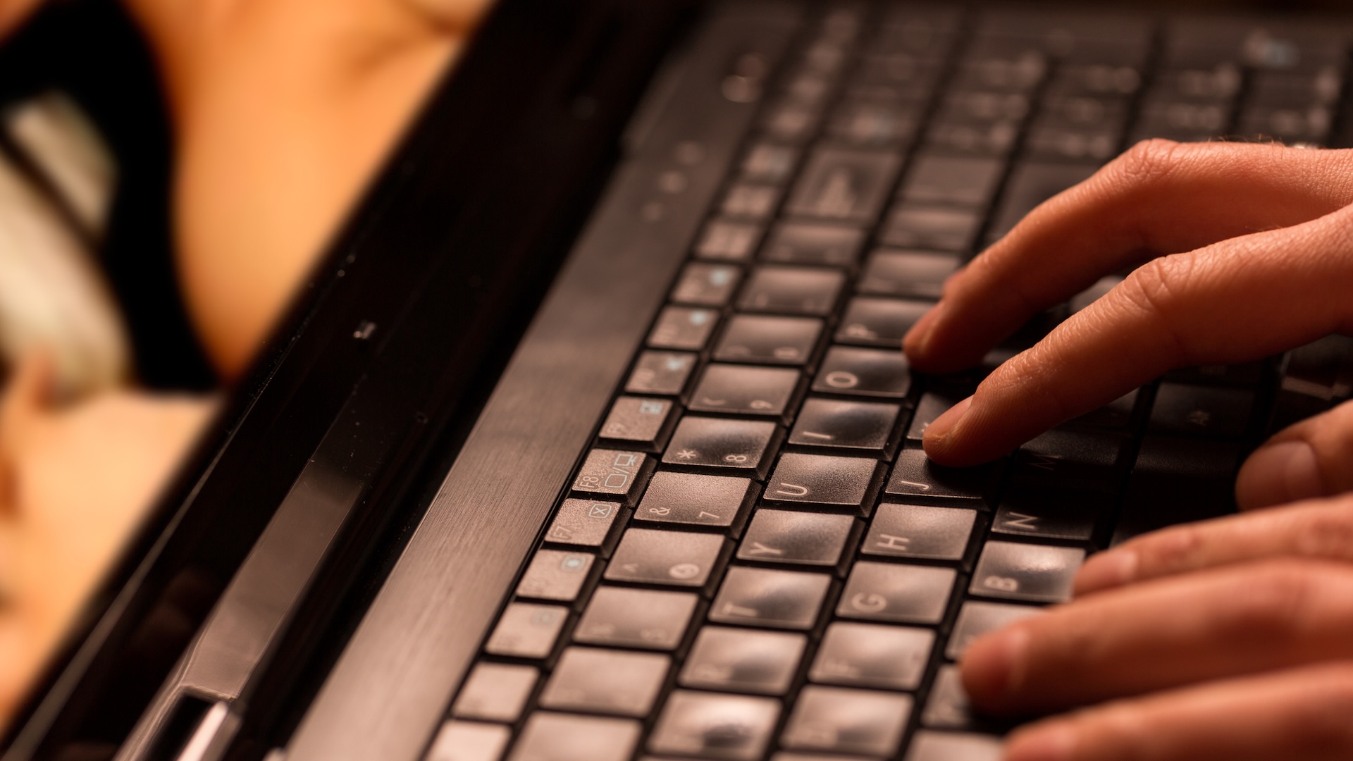 A close-up of hands typing on a laptop keyboard with a blurred background.