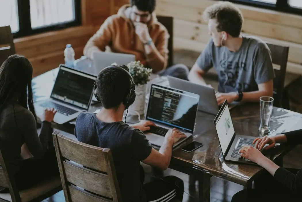Several young people work on laptops in a shared workspace.