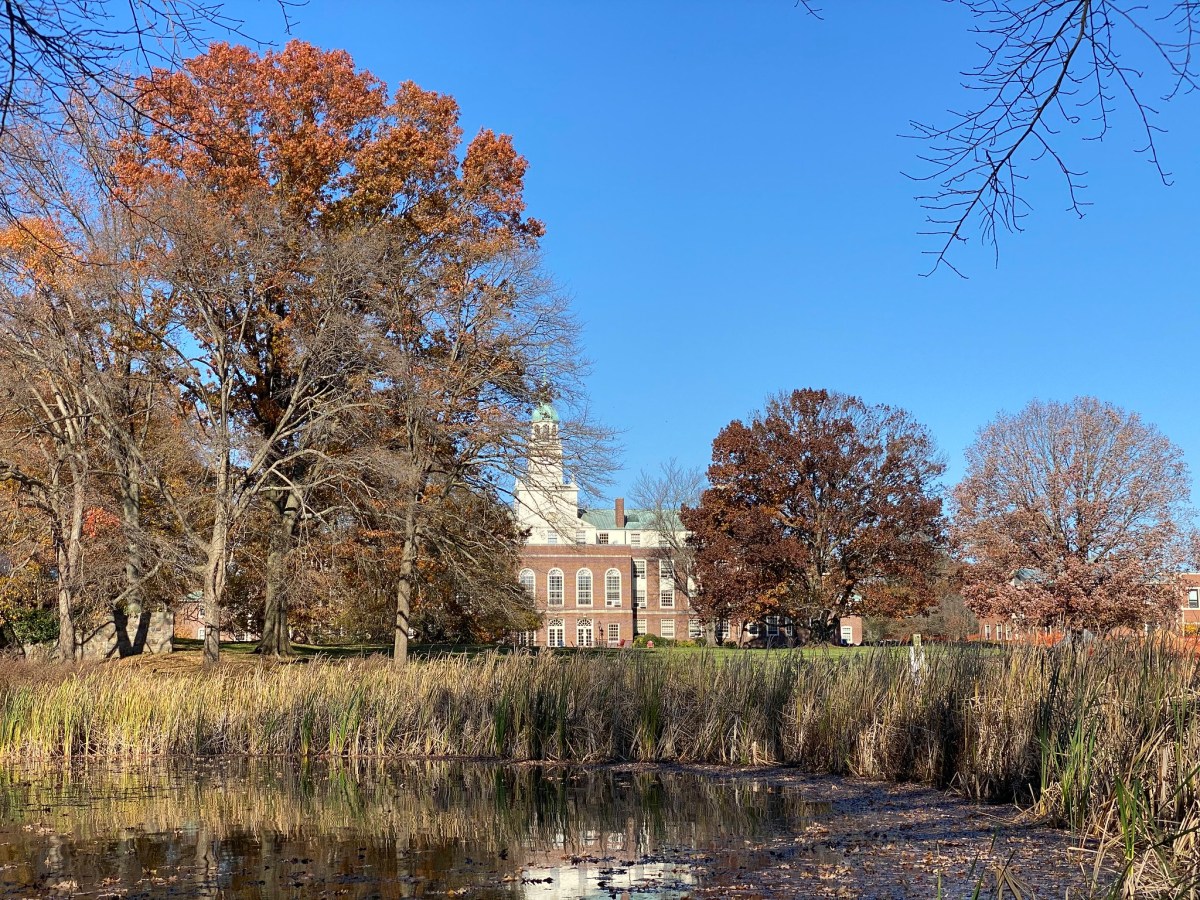 A wooded lake, with a stately Georgian brick building visible in the distance.