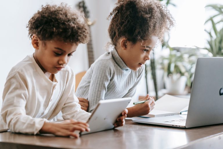 Two children learning together on a tablet and laptop